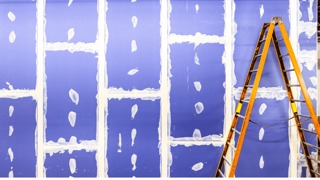 Purple drywall panels taped and mudded with an orange ladder on site.