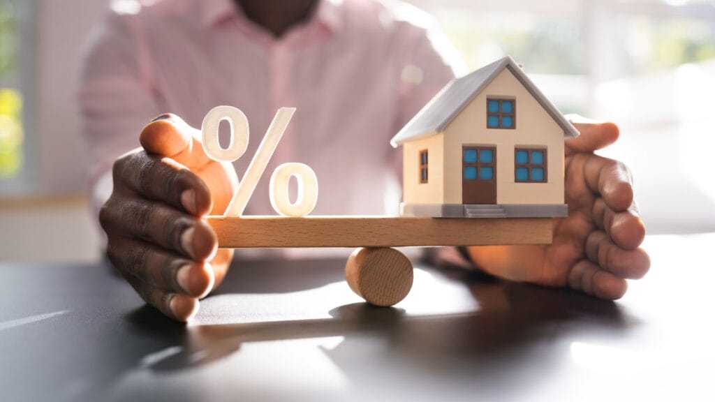 Homebuyer balancing a house model and percentage symbol demonstrating how does a rate buydown work to lower payments.