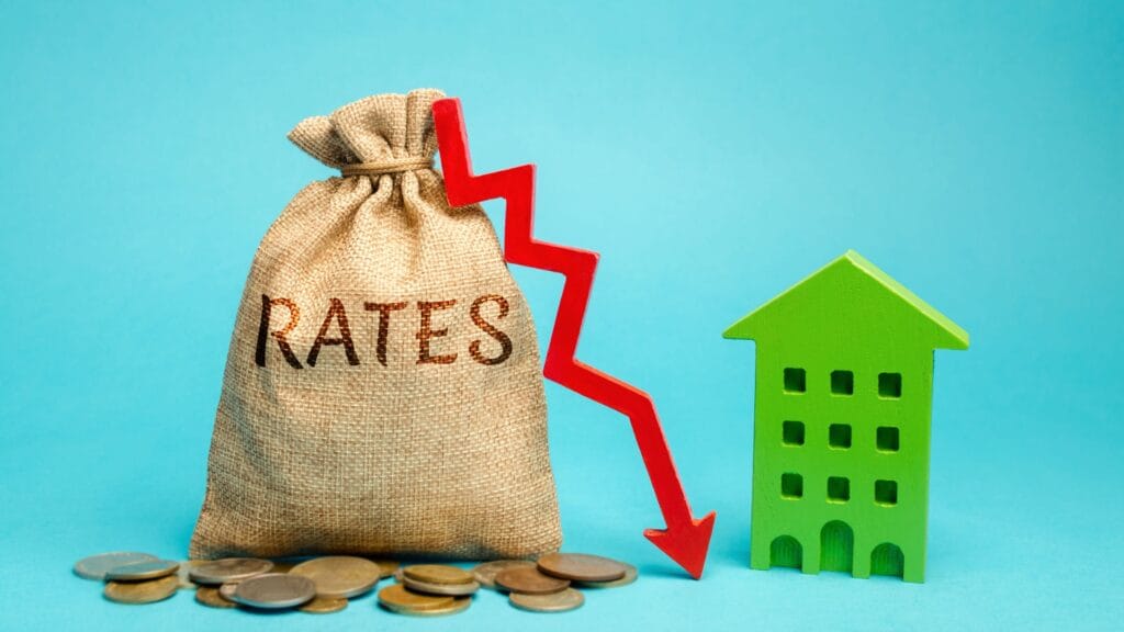 Bag labeled rates with downward red arrow next to house model showing how does a rate buydown work to reduce mortgage costs.